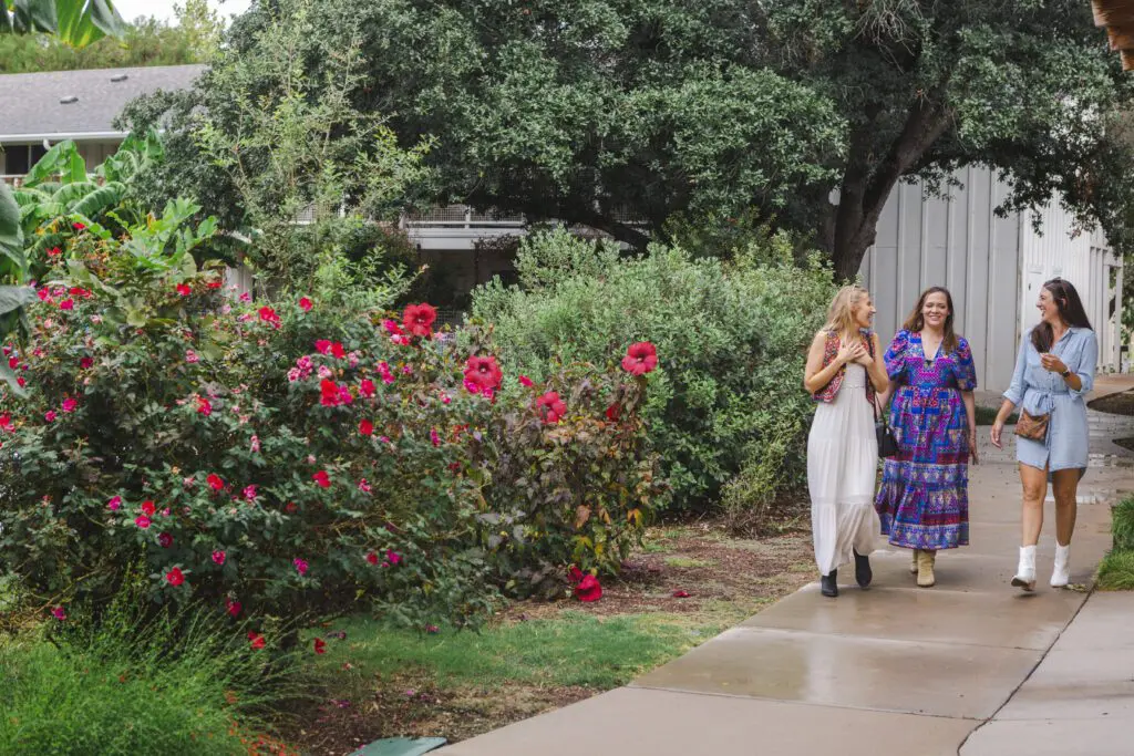 Two women walking and chatting beside blooming flowers at the Stagecoach Inn in Salado, Texas.